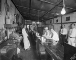 Men sitting at counter and workers stand nearby in an unidentified cafe by Basil Clemons 1887-1964