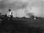 People watching a football game with smoke in the background by Basil Clemons 1887-1964