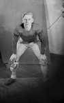 A man in a squatting pose and wearing a football uniform by Basil Clemons 1887-1964