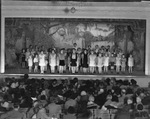 A large group of girls performing on a stage in an auditorium by Basil Clemons 1887-1964