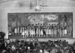 A large group of girls performing on a stage in an auditorium by Basil Clemons 1887-1964