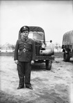 A man posing in a United States Army uniform in front of Army vehicles and tents in the background by Basil Clemons 1887-1964