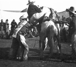 A cowboy assists another cowboy onto a horse by Basil Clemons 1887-1964