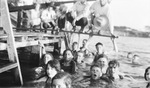 A group of swimmers poses in the water around a dock by Basil Clemons 1887-1964