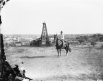 A cowboy rides a horse while in front of an oil derrick by Basil Clemons 1887-1964