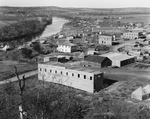 A small town, much of it under construction, along the banks of a river by Basil Clemons 1887-1964