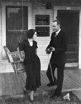 A male violinist and a woman standing on the front porch of a building by Basil Clemons 1887-1964