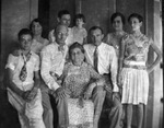 An extended family, all dressed in white or very light-colored clothing, posing around a sofa by Basil Clemons 1887-1964