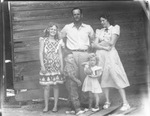 A family standing by a barn by Basil Clemons 1887-1964