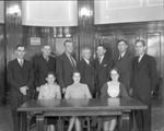 A group of men and women standing or seated at a wooden table by Basil Clemons 1887-1964