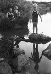 A child standing on a rock surrounded by water by Basil Clemons 1887-1964