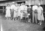 A large family standing in front of a barn by Basil Clemons 1887-1964