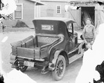 A young man stands in a driveway beside a house and next to a car/truck with a wooden cargo bed, Breckenridge, Texas by Basil Clemons 1887-1964