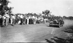 People stand on side of road as a driver in an open-top race car passes by Basil Clemons 1887-1964