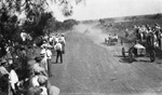 People stand on either side of a road watching an auto race as four cars come into view by Basil Clemons 1887-1964