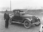 Man stands next to parked car that has an AAA insignia attached to the radiator grille by Basil Clemons 1887-1964