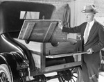 A man shows the wooden trunk of an automobile, by Basil Clemons 1887-1964