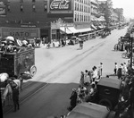 Crowds lined along a wide street, watching a circus parade by Basil Clemons 1887-1964