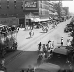 Crowds lined along a wide street, watching a circus parade by Basil Clemons 1887-1964