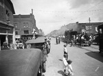 Crowds lined along a street, watching a circus parade by Basil Clemons 1887-1964