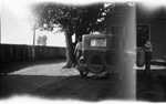 Two people stand near a car parked beside a house by Basil Clemons 1887-1964