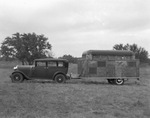 A four-door car with a large covered trailer attached at the rear by Basil Clemons 1887-1964