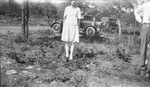 Woman wearing a dress and pearls pose with cars parked behind by Basil Clemons 1887-1964