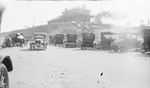 Several cars are parked on a dirt lot at the base of a hill by Basil Clemons 1887-1964