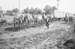 A team of horses pulling a wagon through a muddy street by Basil Clemons 1887-1964