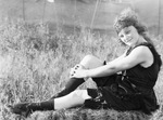 Female circus performer dressed in a black frilly costume sits on the grass, Breckenridge, Texas by Basil Clemons 1887-1964