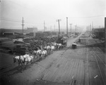 Team of eight horses pulling a circus wagon next to large stacks of lumber beside the railroad tracks, Breckenridge, Texas by Basil Clemons 1887-1964