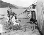 Circus; two monkeys dressed in clothes riding a bicycle-built-for-two near a circus tent, Breckenridge, Texas by Basil Clemons 1887-1964