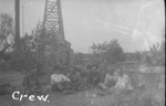 Oil field work crew sitting on the ground next to an oil derrick by Basil Clemons 1887-1964