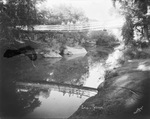 "Lover's Retreat" with people standing on a pedestrian bridge looking over a calm and serene stream where the bridge is reflected in the water, Breckenridge, Texas by Basil Clemons 1887-1964