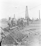 Ballard and Smallwood Pipeline crew stand next to ditch dug to lay pipeline in an oil field with oil derricks; H. and S. Oil Well #67, Block 41 in background, near Breckenridge, Texas. by Basil Clemons 1887-1964