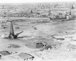 Air view of small community of buildings scattered among numerous oil derricks with railroad track running through landscape, undated by Basil Clemons 1887-1964