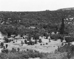 Oil field near Breckenridge, Texas; tree covered hill with wooden structures near an oil derrick by Basil Clemons 1887-1964