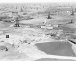 Aerial view of large oil field with numerous derricks on the landscape and a containment pond in foreground by Basil Clemons 1887-1964