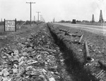 Pipeline being laid along road that cuts through an oil field; sign advertises Oil Field Lumber Co., Joe Stubblefield, contractor, Breckenridge, Texas by Basil Clemons 1887-1964