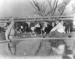 Two men sit on the edge of a water tank with a small herd of cattle behind them on an unidentified ranch in Stephens County, Texas by Basil Clemons 1887-1964