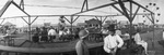 People seated with a circus fairground and amusement rides in the background, Breckenridge, Texas by Basil Clemons 1887-1964