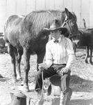 Man in cowboy attire sits next to unsaddled horse, Breckenridge, Texas by Basil Clemons 1887-1964