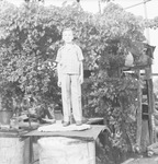 Young boy standing on a large metal container in front of a grape arbor by Basil Clemons 1887-1964