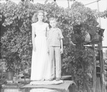 Young woman and boy standing on a large metal container in front of a grape arbor by Basil Clemons 1887-1964