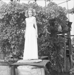 Young woman standing on a large metal container in front of a grape arbor by Basil Clemons 1887-1964