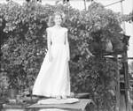 Young woman standing on a large metal container in front of a grape arbor by Basil Clemons 1887-1964