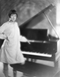 Young woman standing in front of a grand piano by Basil Clemons 1887-1964