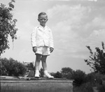 Young boy standing and wearing white socks, shoes, jacket and shorts by Basil Clemons 1887-1964