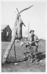 Barney Holland holding a gun beside the carcass of a deer following a hunting trip