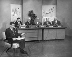 Five men seated at table with microphones in a TV studio